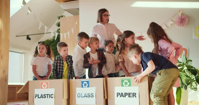 children in a school preparation club lay out different types of garbage in the right box for plastic for glass and for paper together with their teacher, a girl with a bob in a white shirt