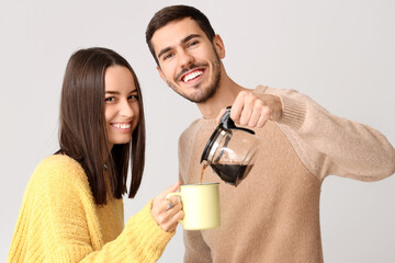 Loving couple in warm sweaters pouring coffee on light background