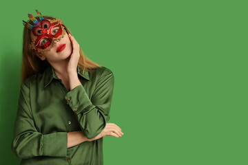 Beautiful young woman in carnival mask on green background