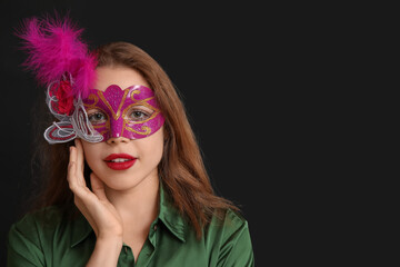 Beautiful young woman in carnival mask on black background