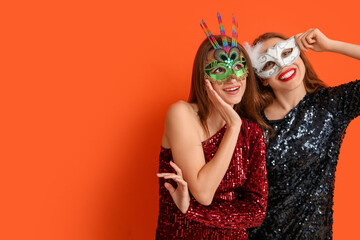 Happy young women in carnival masks on orange background - obrazy, fototapety, plakaty