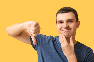 Handsome displeased man after shaving showing thumb-down gesture on yellow background