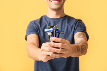 Handsome young man with razors on yellow background