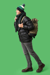 Young man in stylish puffer jacket and scarf with bag on green background