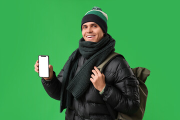 Young man in stylish puffer jacket with mobile phone and bag on green background