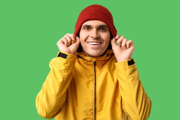 Young man in yellow stylish jacket and hat on green background