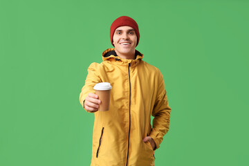 Young man in yellow stylish jacket and hat with paper cup of coffee on green background