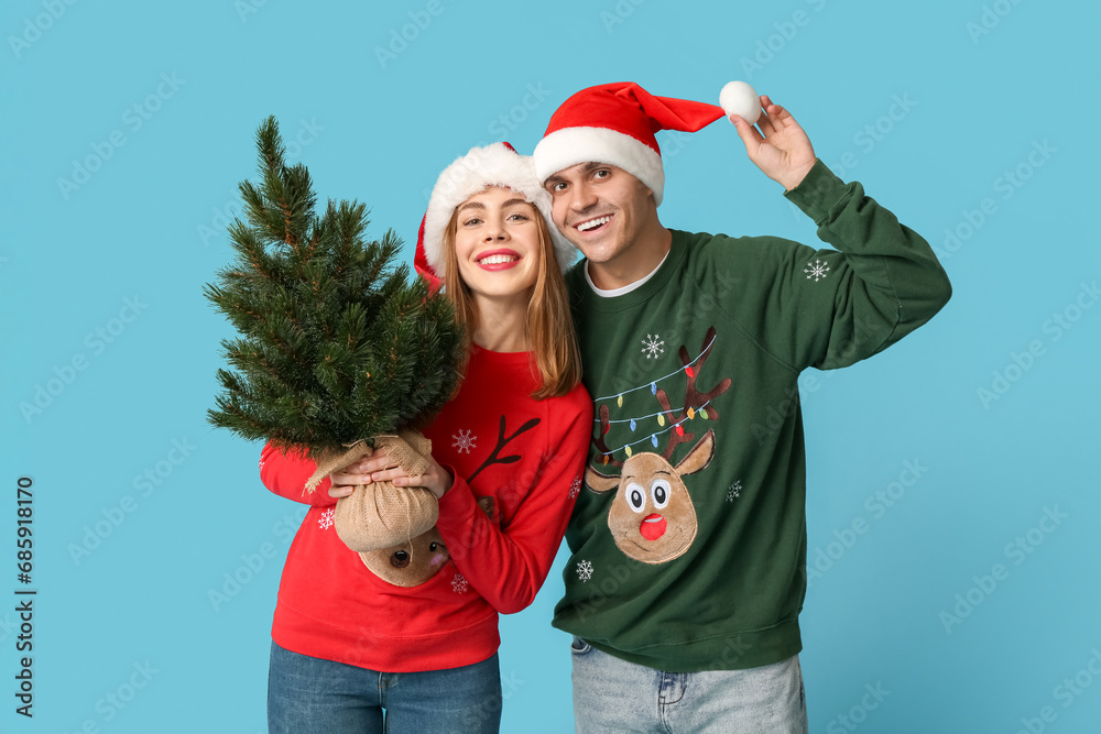 Canvas Prints Happy young couple in Santa hats with Christmas tree on blue background