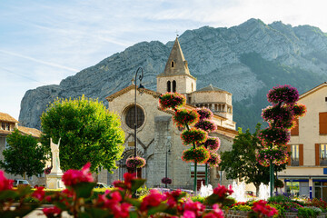 Scenic cityscape of Sisteron overlooking fountain in brightly blooming flowers in front of medieval...