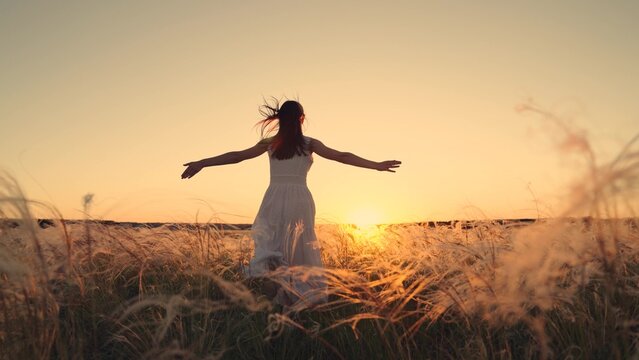 Free girl runs happily through meadow in grass in rays of sunset. Concept of female dreams, success, travel, flight. Young woman holding her arms to sides runs across field in sun. Happy running girl