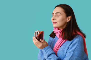 Beautiful young woman in scarf with glass cup of hot mulled wine on blue background