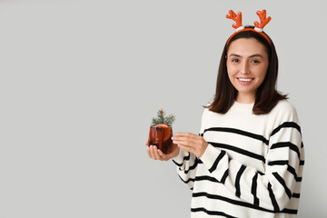 Happy young woman in reindeer horns with glass of hot mulled wine on grey background