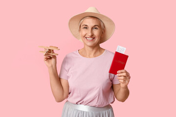 Mature woman with passport and wooden airplane on pink background. Travel concept