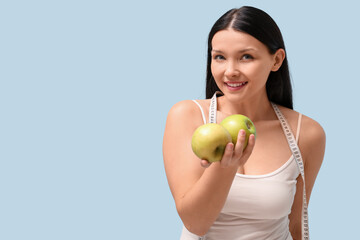 Beautiful young woman with measuring tape and fresh apples on blue background. Weight loss concept