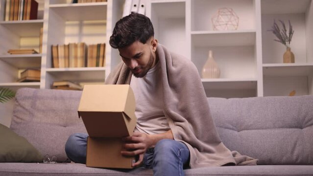 Handsome young bearded man received parcel satisfied with shopping in online internet store looking into box at home Happy customer rejoice with purchase order indoors