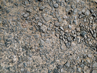 Small cinder stones lie on a dirt road, top view in the rays of the midday sun.