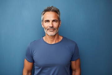Handsome middle-aged man standing in front of a blue background wall.