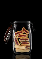 Fruit Newton cookies in a glass storage or canning jar isolated on black with reflection, with lid...