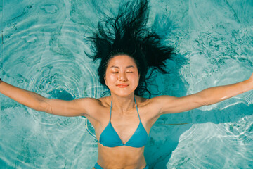 Young asian woman relaxing in the water, Beautiful girl relaxing at overwater infinity pool luxury resort. Spa, wellness, swimming.