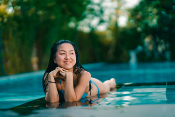 Young asian woman relaxing in the water, Beautiful girl relaxing at overwater infinity pool luxury resort. Spa, wellness, swimming.