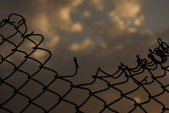 Looking up at a chain link fence with blue sky and clouds. wire fence. Chain link fence see sky. Opening in metallic fence. red sky. Challenge. breakthrough concept