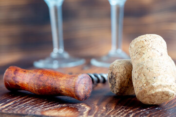 Two wine corks close-up, corkscrew and glass legs in the background, on a wooden background