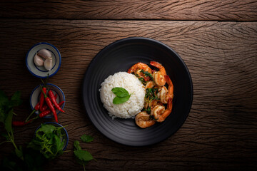 Stir-fried shrimp with basil Thai street food arranged on a black plate Spicy Thai food placed on a wooden table. Top view.