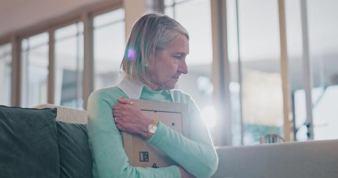 Sad senior woman, hug photo and thinking with grief, lost love and broken heart on living room sofa in home. Elderly lady, picture frame and depression for death, mourning and memory on lounge couch