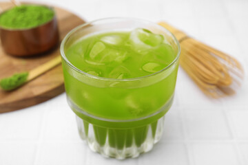 Glass of delicious iced green matcha tea on white tiled table, closeup