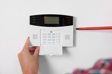 Man installing home security alarm system on white wall indoors, closeup
