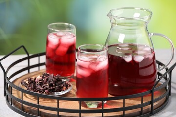 Refreshing hibiscus tea with ice cubes and dry roselle flowers on white wooden table against...
