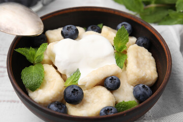 Bowl of tasty lazy dumplings with blueberries, sour cream and mint leaves on white wooden table,...