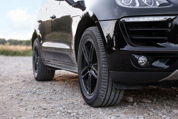 Modern black car parked on rubble road outdoors