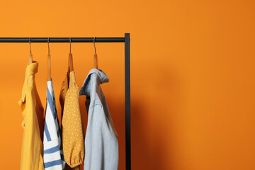 Rack with stylish clothes on wooden hangers against orange background, space for text