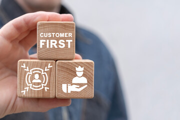 Man holding wooden blocks with icon sees inscription: CUSTOMER FIRST. Client centricity business orientation. Customer first concept. VIP client servcie. Customer relationship management (CRM).