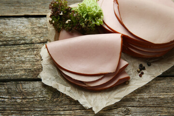 Slices of delicious boiled sausage with lettuce and spices on wooden table, above view