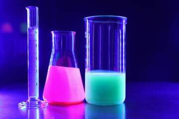 Laboratory glassware with luminous liquids on table against dark blue background