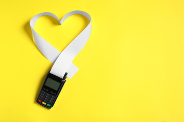 Payment terminal and heart made of thermal paper for receipt on yellow background, top view. Space...