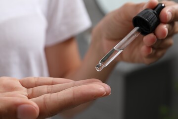 Woman applying cosmetic serum onto her finger on blurred background, closeup
