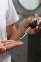 Woman applying cosmetic serum onto her finger on blurred background, closeup