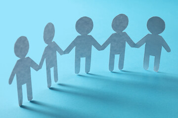 Teamwork concept. Paper figures of people holding hands on light blue background