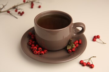 Brown cup with hawthorn tea and berries on beige table