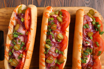 Tasty hot dogs with green onion, tomato, pickles and sauce on wooden table, top view