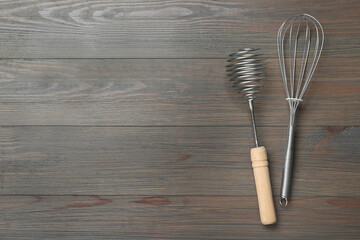 Two metal whisks on wooden table, top view. Space for text