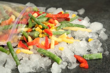 Zip bag with different frozen vegetables and ice on grey table, closeup
