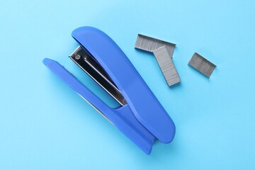 Stapler with staples on light blue background, flat lay