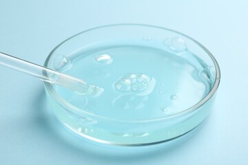 Petri dish with liquid sample and pipette on light blue background, closeup