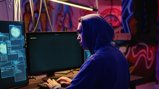 Asian hacker hiding in underground bunker, looking over his shoulder and feeling anxious after stealing data from victims using computer virus, scared about being caught by police