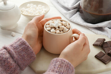 Woman holding cup of aromatic hot chocolate with marshmallows at table, closeup