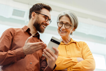 Portrait of bearded ceo businessman holding mobile phone, talking with senior woman colleague